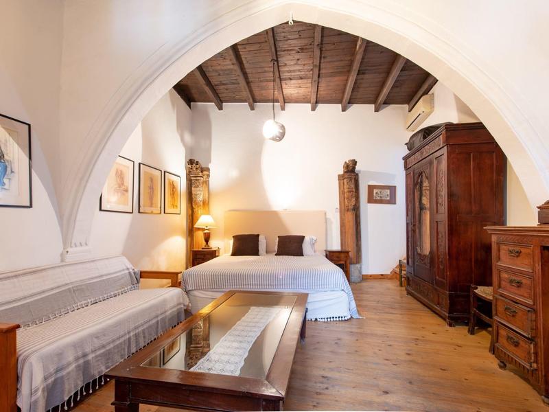 Helles Schlafzimmer mit Doppelbett, Holzmöbeln und Sitzbank unter einem gewölbten Deckenbalken.