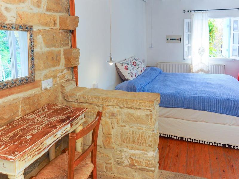 Gemütliches Hotelzimmer mit Steinmauer, Holztisch, Stuhl und Bett mit blauer Tagesdecke.