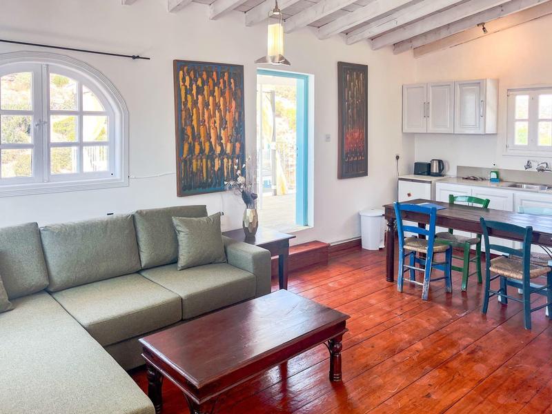 Helles Wohnzimmer mit grauem Sofa, Holztisch und angrenzender Küche mit blauem Essbereich.