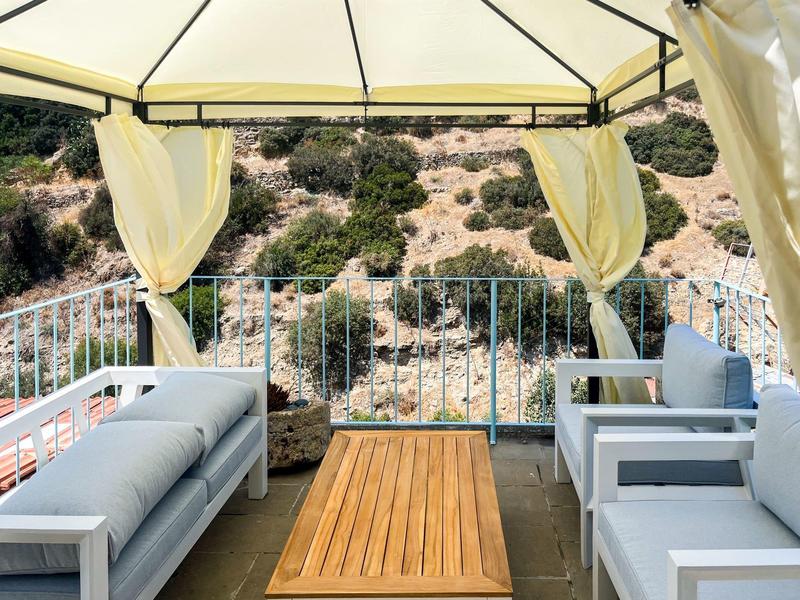 Gemütliche Lounge mit weißen Sofas und Holztisch unter einem Sonnenschutz mit Blick auf felsige Landschaft.