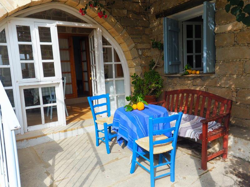 Gemütliche Terrasse mit blauem Tisch, Stühlen und rustikalem Holzbett an Steinwand.