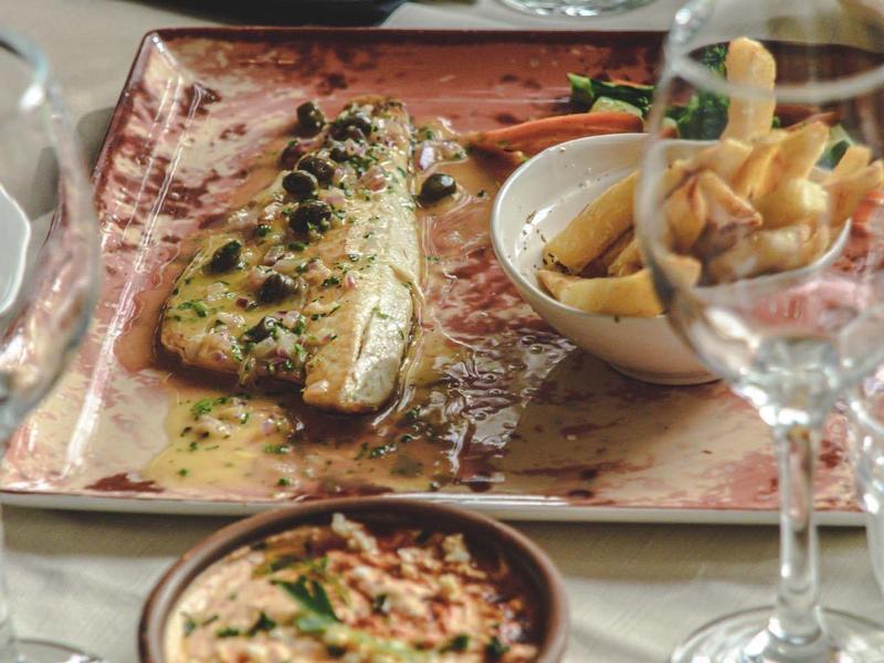 Ein gedeckter Tisch mit mediterranen Gerichten, darunter gegrillter Fisch und Dips.