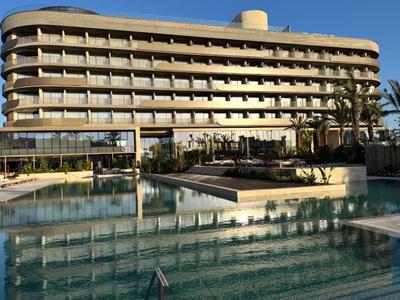 Nowoczesny budynek hotelowy z wieloma balkonami i dużym basenem na pierwszym planie.