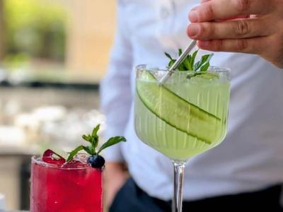 Barman przygotowuje dwa koktajle, zielony z plasterkami ogórka i czerwony z jagodami.