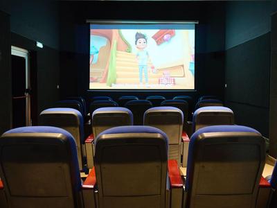 Malý kinosál s řadami polstrovaných sedadel promítá animovaný film na plátně.