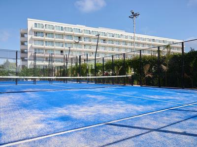 Modré hřiště na paddle tenis před moderní hotelovou budovou pod modrou oblohou.