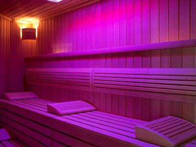 Dřevěná sauna s vícestupňovými lavicemi a nepřímým fialovým osvětlením.