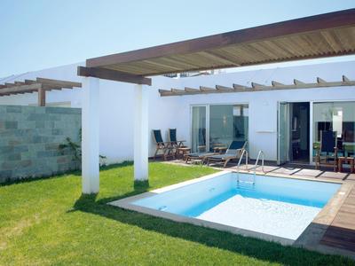 Bungalow moderne avec petite piscine, chaises longues et terrasse en bois dans le jardin.