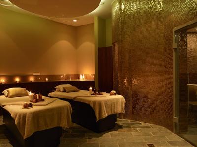 Salle de spa accueillante avec deux tables de soins, éclairage chaleureux et décoration élégante.