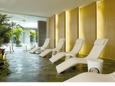 Chaises longues modernes dans un espace bien-être lumineux avec sol en pierre et plantes.