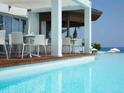 Piscina exterior moderna con muebles blancos en una terraza con vista al mar.