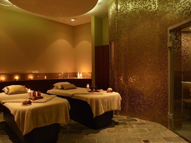 Salle de spa accueillante avec deux tables de soins, éclairage chaleureux et décoration élégante.