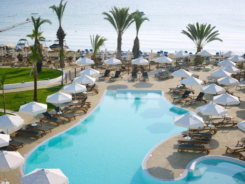 Grande piscine d'hôtel avec parasols blancs et chaises longues au bord de la mer.