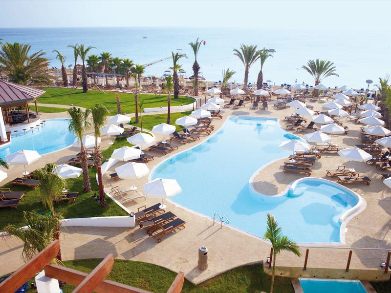 Grand piscine extérieure avec chaises longues et parasols à côté des palmiers sous un ciel bleu.