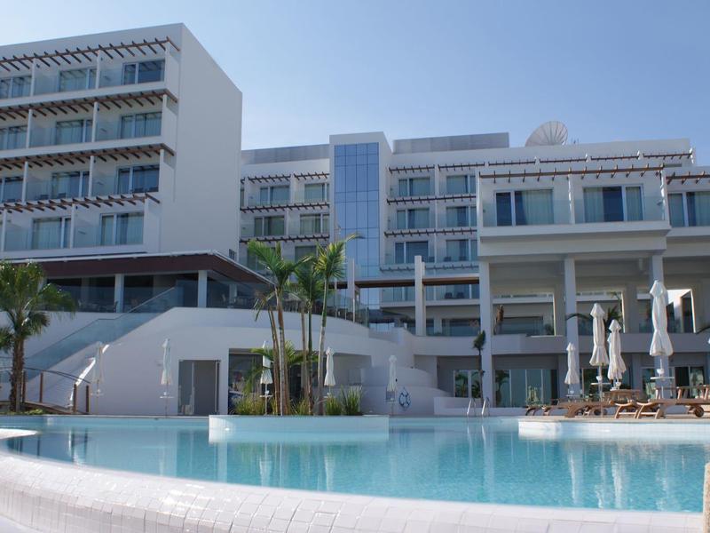 Hôtel moderne avec piscine extérieure claire et parasols sous un ciel bleu.