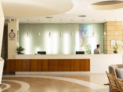 Recepción de hotel con suelo color crema y mostrador largo de madera y material blanco.