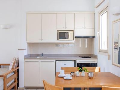 Cocina luminosa con sillas de madera, mesa de comedor, microondas y armarios blancos en una habitación de hotel.