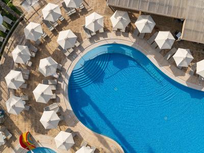 Piscina moderna en hotel con sombrillas blancas y tobogán colorido.