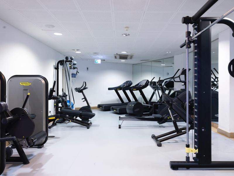 Moderner Fitnessraum mit mehreren Laufbändern, Hanteln und Kraftmaschinen in hellen Farben.