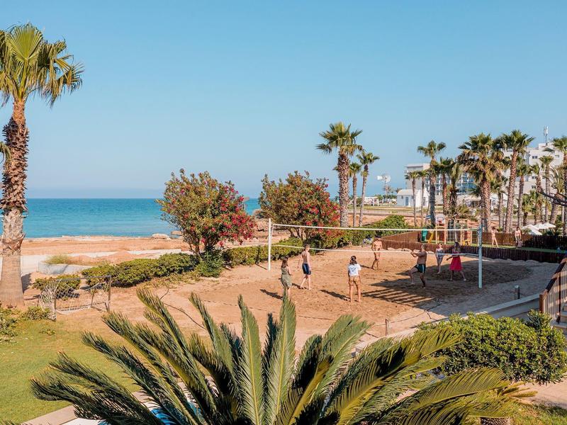 Strandpark mit Palmen, Spaziergängern, Sandweg und blauem Meer im Hintergrund bei klarem Himmel.