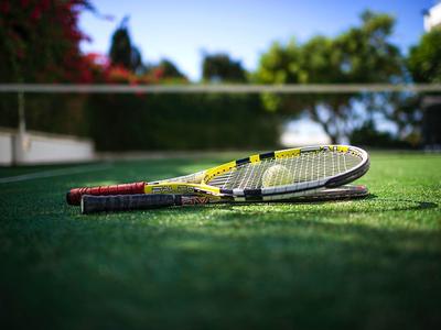 Zwei Tennisschläger liegen auf grünem Tennisplatz unter blauem Himmel.