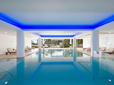 Moderner Innenpool mit blauer Beleuchtung, Liegen und großen Fenstern zum Außenbereich.