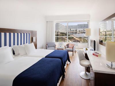 Modern eingerichtetes Hotelzimmer mit zwei Betten, blauen Decken und großem Fenster mit Blick.