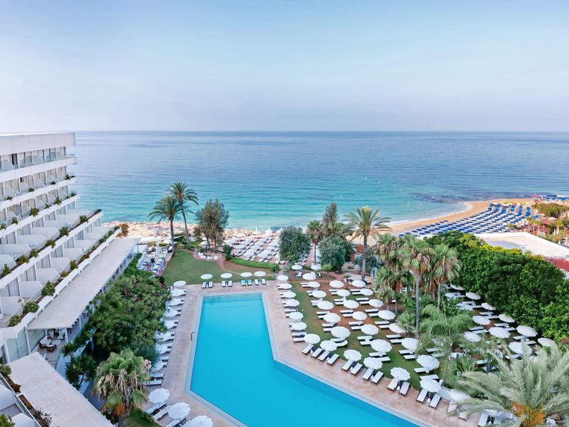 Hotelanlage mit großem Pool, Sonnenliegen und Meerblick an einem sonnigen Tag.