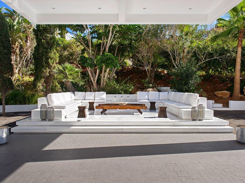 Moderner Außenbereich mit weißen Sofas und Holz-Couchtischen, umgeben von üppigem Grün.