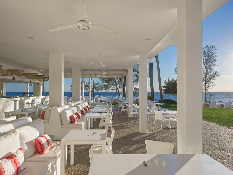 Offener, moderner Hotelbereich mit weißen Möbeln und Blick auf das Meer bei Sonnenuntergang.