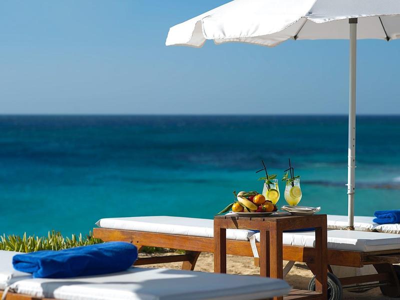 Pflegeleichte Liegestühle und Sonnenschirm am Meer mit Getränken auf dem Tisch.