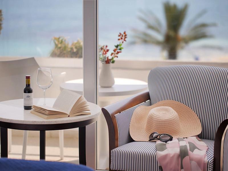 Gemütliche Sitzecke mit Stuhl, Tisch, Weinflasche, Sonnenhut und Meerblick.