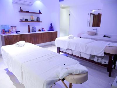 Ruhiger Massageraum mit zwei weißen Liegen, Holzmöbeln und sanfter Beleuchtung.