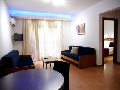 Helles Wohnzimmer mit Holzsofas, Tisch, Vorhängen und offenem Zugang zu einem weiteren Raum.