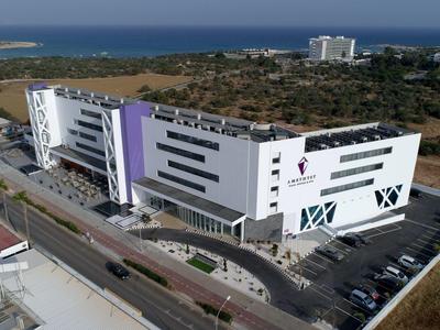 Modernes, weißes Bürogebäude mit lila Akzent, parkplatzseitig an einer Straße, umgeben von Feldern und Meer.