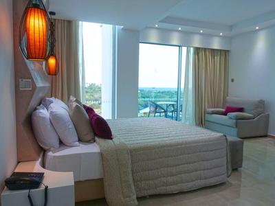 Helles Schlafzimmer mit großem Fenster, Doppelbett, gemütlichem Sofa und modernen Lampen an der Wand.