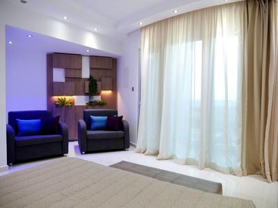 Helles Wohnzimmer mit zwei blauen Sesseln, Vorhängen und modernem Regal mit Dekoration.