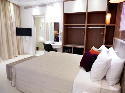 Modernes Schlafzimmer mit großem Bett, weißen Vorhängen, Holzregalen und einem TV an der Wand.