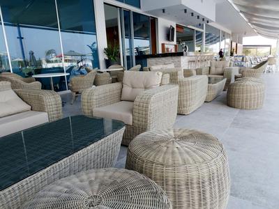 Moderne buitenruimte met gevlochten stoelen en tafels voor een gebouw met glazen gevel.