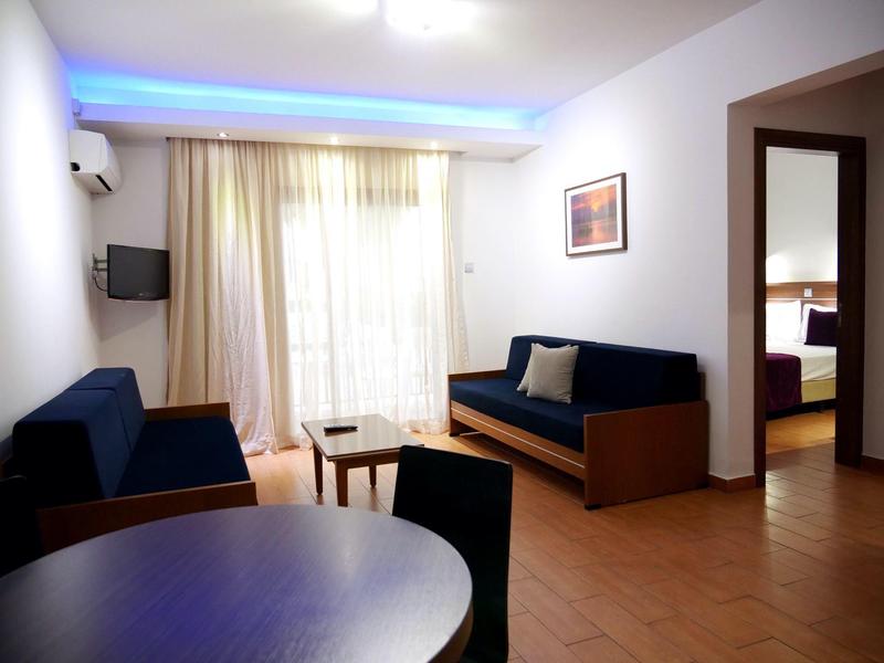 Helles Wohnzimmer mit Holzsofas, Tisch, Vorhängen und offenem Zugang zu einem weiteren Raum.