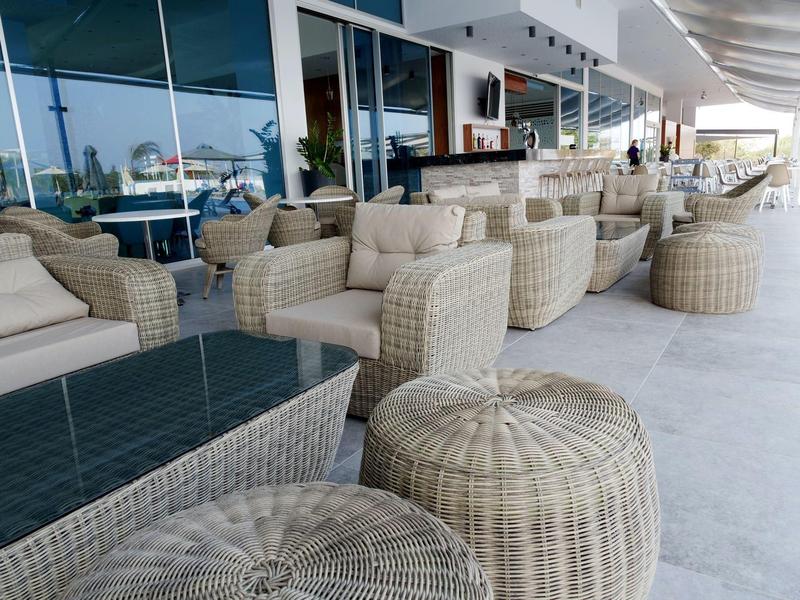 Außenbereich mit geflochtenen Sitzmöbeln und Tischen vor einem Glasgebäude am Tag.