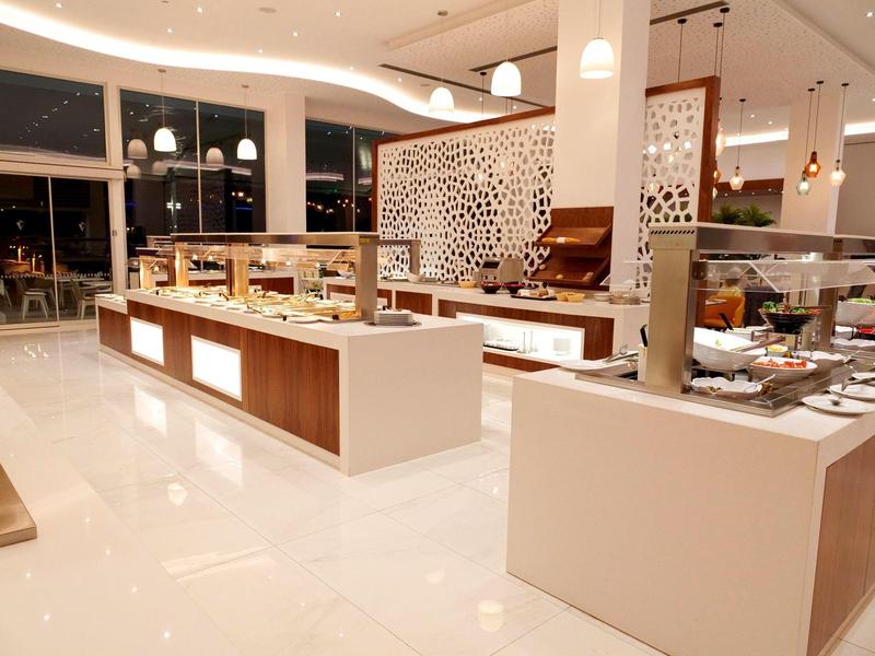 Moderner, heller Buffetbereich mit weißen Theken, Glasvitrinen und warmen Deckenlampen.