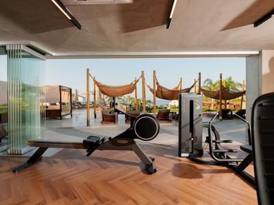 Moderner Fitnessraum mit Blick auf einen Balkon mit Sonnensegeln und mediterranen Pflanzen.
