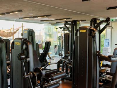 Moderner Fitnessraum mit schwarzen Trainingsgeräten und Holzparkettboden in einem Hotel.