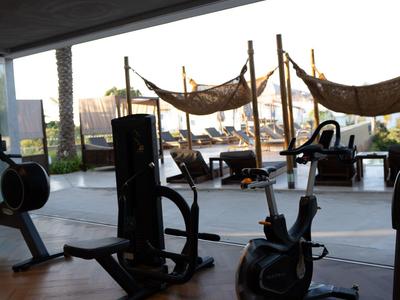 Indoor-Fitnessraum mit modernen Trainingsgeräten und Blick auf Fenster mit Hängematten außen.