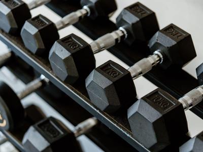 Reihe schwarzer sechseckiger Hanteln auf einem Halter in einem Fitnessraum.