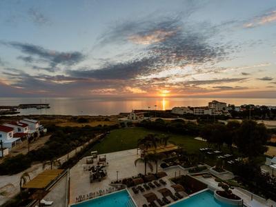 Blick auf einen Sonnenuntergang über einem Hotelpool und angrenzenden Gebäuden nahe dem Meer.