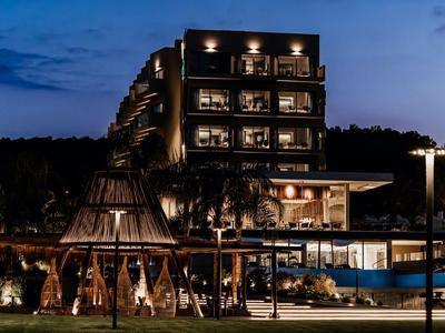 Ein beleuchtetes modernes Hotelgebäude bei Nacht mit Pool und einer hölzernen Lounge im Vordergrund.