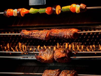 Mehrere Fleischspieße und ein bunter Gemüse-Spieß werden auf einem Grill im Freien zubereitet.