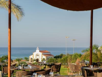 Offenes Restaurant mit Blick auf das Meer und ein weißes Gebäude unter blauen Himmel.